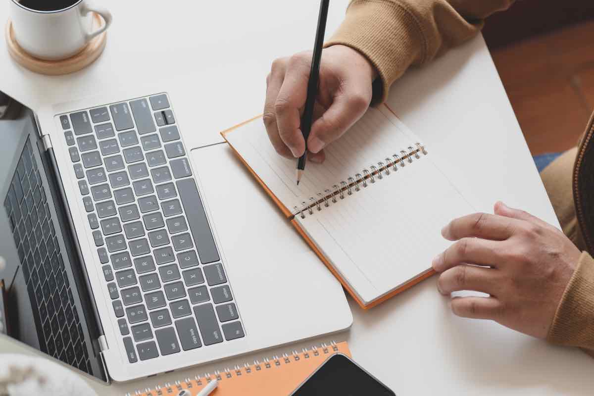 Un uomo prende appunti davanti a un pc portatile