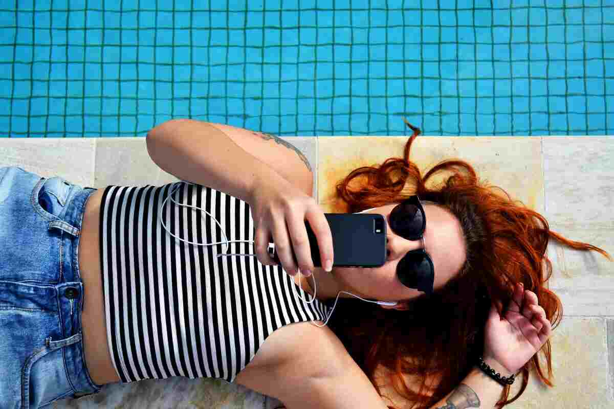 ragazza usa cellulare sdraiata a bordo piscina